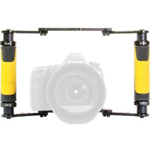 A DSLR camera mounted inside a bright yellow and black Ikan Dragonfly camera rig, featuring two side handles for handheld stabilization.
