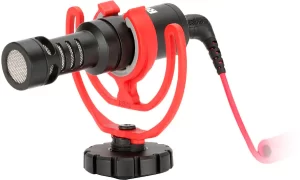 Røde compact on-camera microphone inside a bright red Rycote Lyre shock mount, connected by a coiled black patch cable.