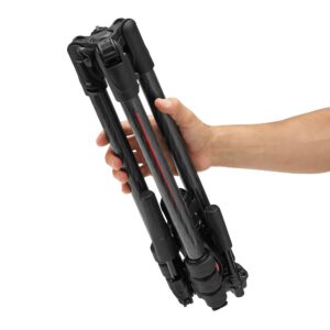 Close-up of a compact, black aluminum Manfrotto Befree tripod folded completely closed into its travel position, being held by a hand.