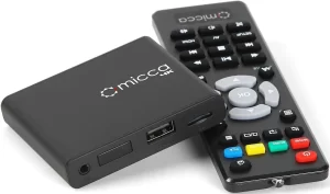 Top-down angled view of a compact, black Micca digital media player, showing its rear panel inputs including HDMI, AV, coaxial, optical audio, and a DC power jack.